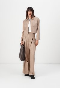 Giacca cropped a righe beige e pantaloni a gamba larga coordinati, abbinati a una maglietta bianca e scarpe nere. Una borsa tote scura viene tenuta in mano.