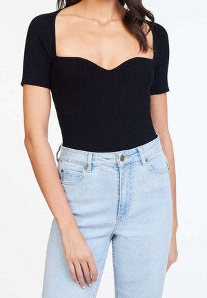 Woman wearing black, short-sleeve, square-neck top tucked into high-waisted, light blue denim jeans with front button and pockets.