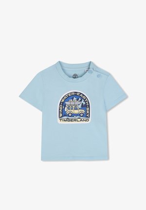 T-shirt en coton bleu clair avec un col rond, des manches courtes et un détail de boutons pression. Présente une impression graphique avec un véhicule et des éléments de la nature.