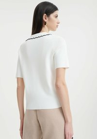 Bílý krátký rukáv top s černým zvlněným límcem, vyrobený z měkkého materiálu, s přiléhavým střihem a čistým, minimalistickým siluetou.