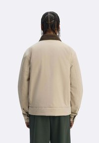 Giacca beige con colletto in velluto a coste marrone, taglio oversize e trama liscia, vista posteriore e maniche larghe.