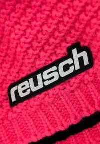 Fuchsia knitted beanie with textured pattern, featuring a black label with white "reusch" text prominently displayed.