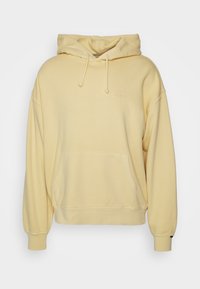 Sudadera amarilla con capucha hecha de tela suave, que cuenta con un bolsillo frontal, cordón ajustable y un pequeño logotipo bordado en el pecho.