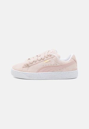 Světlé růžové semišové tenisky Puma Suede s tlustými tkaničkami, bílou podrážkou a zlatým logem Puma na boku.