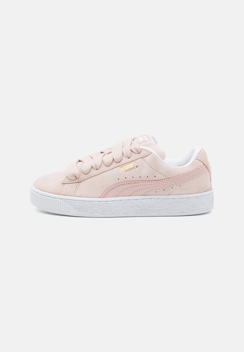 Baskets Puma Suede en daim rose clair avec lacets épais, semelle blanche et logo Puma doré sur le côté.