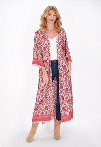 Pituu long floral kimono vaaleanpunaisena ja vihreänä, jossa on kuviollisia yksityiskohtia ja avoin etuosa. Yhdistetty valkoisen paidan ja sinisten farkkujen kanssa, käytetty beigeillä saappailla.
