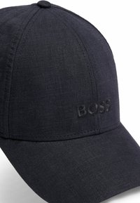 Dark blue cap made of textured fabric with a curved brim. Features an embroidered "BOSS" logo in matching color, with a rounded top.