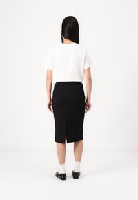 Falda lápiz negra con una abertura trasera, combinada con una camiseta blanca de manga corta. Tejido texturizado y diseño ajustado. Sin herrajes visibles.