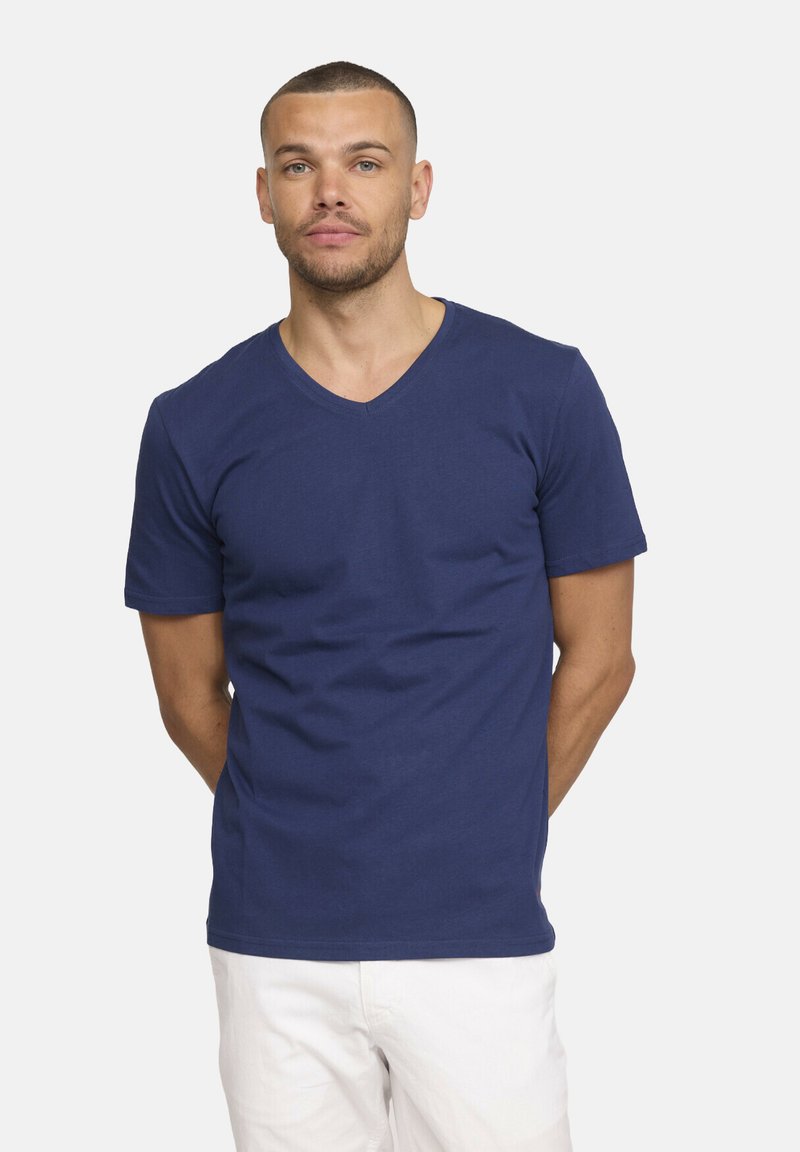 T-shirt en coton bleu marine à col en V et à manches courtes. Présente un design simple et est associé à un short de couleur claire.