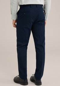 Pantaloni texturați de culoare bleumarin cu o croială slim și dungi fine, având buzunare la spate și o talie netedă, asortați cu pantofi negri.