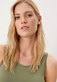 Olivgrünes Tanktop mit Rundhalsausschnitt, aus weichem, glattem Stoff. Das Model hat glattes, blondes Haar und ein natürliches Makeup in neutralen Tönen.