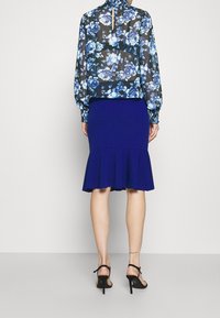 Floral sheer blouse with blue and black pattern, high neckline, elastic cuffs; paired with a fitted royal blue skirt featuring a flared hem.