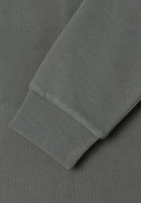 Tela de algodón gris con puño acanalado. La textura es suave y elástica, con un color sólido y uniforme sin patrones ni detalles.