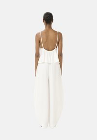 Witte jumpsuit met een vloeiende silhouet, spaghettibandjes, gelaagde ruches detail aan de achterkant en wijde pijpen. Zachte, gestructureerde stof.