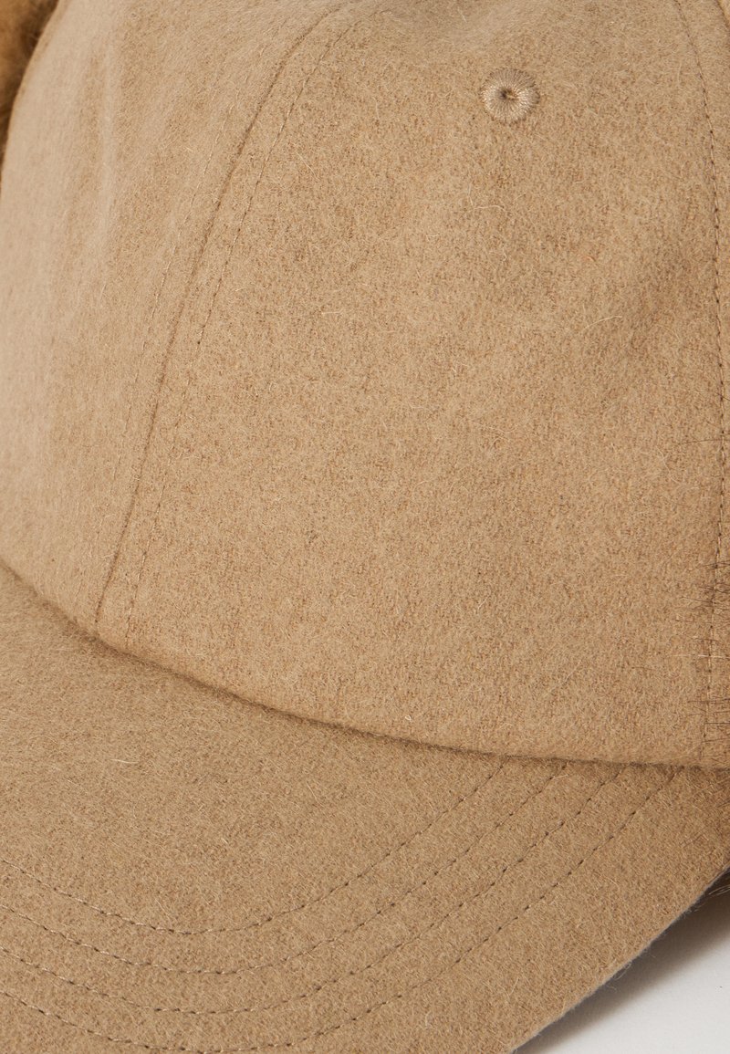 Beige wool baseball cap with visible stitching and fabric texture, showing the front panels and curved brim.