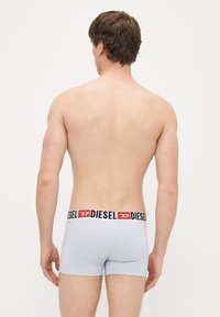 Gaiši zili bokseršorti ar melnu un sarkanu Diesel logotipa jostu, ar gludu audumu un pieguļošu dizainu, redzami no mugurpuses.