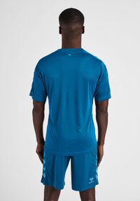 Blå atletisk t-shirt och shorts, tillverkade av ett glatt, lätt tyg. Har korta ärmar och en diskret logotyp på shortsen.