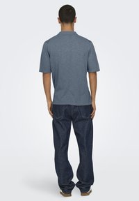 Camiseta corta gris de manga corta con cuello redondo, combinada con jeans de mezclilla oscuros de corte suelto. Diseño simple, sin patrones o acentos notables.