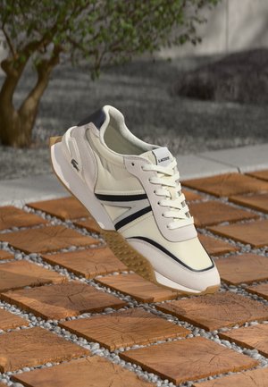 Licht crème sneakers met zwarte accenten, textuurmaterialen, vetersluiting en een rubberen zool. Het ontwerp heeft een gladde en sportieve uitstraling.