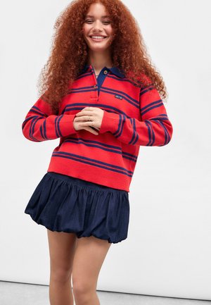 Maglione a righe rosse e navy con colletto, maniche lunghe e polsini a coste, abbinato a una gonna svasata in denim scuro.