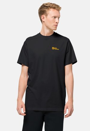 T-shirt nera a maniche corte in cotone, con un piccolo logo giallo di Jack Wolfskin sul petto. Design semplice e pulito con una vestibilità relax.