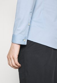 Camicia azzurra chiara a maniche lunghe con polsini abbottonati, realizzata in tessuto morbido, caratterizzata da un design semplice e pulito e un orlo dritto.