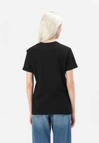 Black cotton t-shirt with short sleeves and a crew neckline, shown from the back, paired with blue denim jeans.