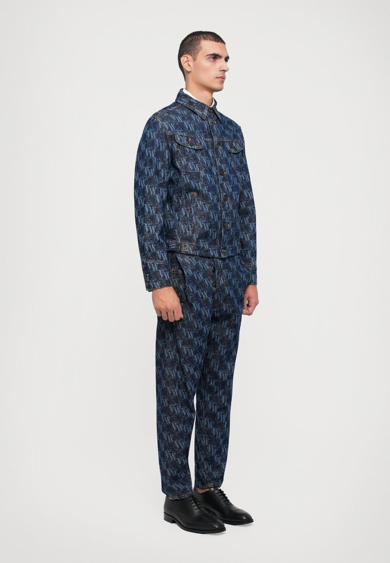 Giacca di jeans e pantaloni coordinati in blu scuro con un design a motivo su tutta la superficie. La giacca presenta un colletto e tasche anteriori, abbinata a scarpe nere.