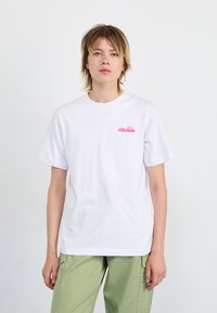 T-shirt en coton blanc avec un petit logo "ellesse" rose sur la poitrine, coupe décontractée et manches courtes. Assorti à un pantalon vert clair.