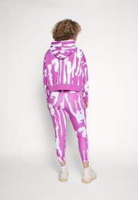 Růžová mikina s bílými abstraktními vzory a zkráceným střihem, v kombinaci s odpovídajícími legínami se stejným vzorem a hladkou texturou.