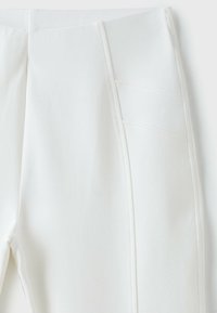 Gros plan d’un pantalon en tissu blanc montrant les détails des coutures et le design des panneaux sur la partie supérieure de la cuisse et la ceinture.