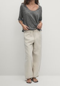 Szara koszula z krótkim rękawem i dekoltem w kształcie łódki, zestawiona z luźnymi beżowymi spodniami z elastycznym pasem i sznurkiem. Dopełnieniem są sandały.