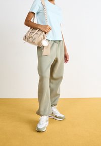 Světle modré tričko s krátkým rukávem, olivově zelené tepláky, bílé a zelené tenisky, béžová křížová taška se zipem a kulatým detailem.