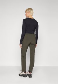 Calças verde-oliva de corte slim, feitas de material leve, com bolsos laterais e uma textura suave, combinadas com sapatos pretos robustos.