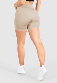 Beige hooggetailleerde shorts van rekbaar materiaal, met een gladde textuur en een aansluitend ontwerp, gecombineerd met witte sneakers en sokken.