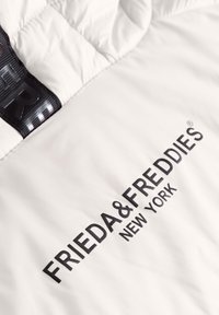 Witte gewatteerde jas met een zwarte logo-opdruk van "FRIEDA & FREDDIES NEW YORK" en een gestructureerde zwarte band. Glad, glanzend materiaal.