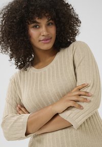 Beige geribbelde gebreide trui met 3/4 mouwen, voorzien van een ronde halslijn en horizontale textuurpatronen.