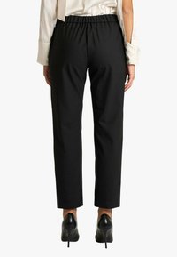 Pantaloni neri a vita alta con cintura elasticizzata e design a gamba dritta. Tessuto strutturato, lunghezza alla caviglia. Indossati con tacchi neri.