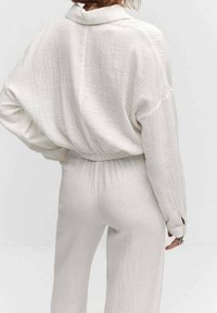 Jasno beżowy, lekki strój o teksturowanym wykończeniu; zawiera luźną bluzkę z kołnierzykiem oraz dopasowane spodnie w talii.