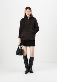 Brun, lurvig fleece-pullover med kvartslång dragkedja och framficka, parat med en svart minikjol och knähöga svarta stövlar.