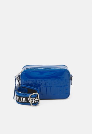 Modrá kabelka přes rameno z lakované kůže s vytlačeným nápisem "VERSACE JEANS COUTURE", zapínáním na zip a odnímatelným popruhem s kontrastním písmem.
