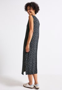 Sleeveless maxi dress in dark navy with a geometric pattern in light gray. Features a back slit and relaxed fit, paired with light sneakers.