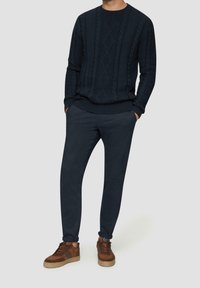 Námořnicky modrý svetr s copánkovým vzorem ve spojení s námořnicky modrými kalhotami se zúženými nohavicemi a hnědými teniskami. Oblečení je vyrobeno z texturované látky a má pohodlný střih.