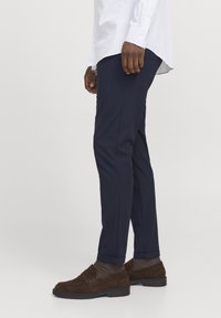 Marineblaues Slim-Fit-Hose aus strukturierter Stoff. Kombiniert mit braunen Wildleder-Mokassins und grau-braunen Socken mit umgeschlagenem Saum.