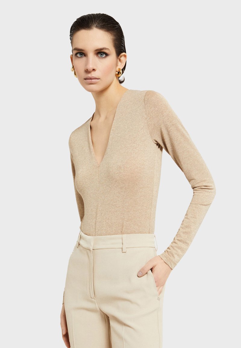 Prilagođeni bodi dugih rukava u metalik bež boji, s dubokim V-izrezom i glatkom teksturom, u kombinaciji s hlačama svijetle bež boje visokog struka.