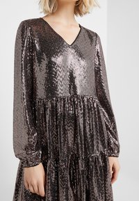 Robe à manches longues en V, en tissu à sequins scintillants dans des tons sombres. Présente un design à niveaux avec des détails froncés à la taille.