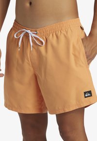 Bañadores de hombre en color naranja claro, fabricados en material sintético, con una cintura elástica, cordón blanco y un parche con el logo en negro.