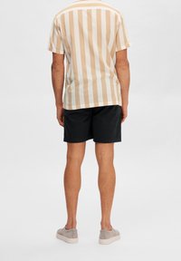Camicetta a maniche corte a righe in beige chiaro e bianco, abbinata a pantaloni corti neri, che mette in risalto un taglio morbido e una texture in cotone.
