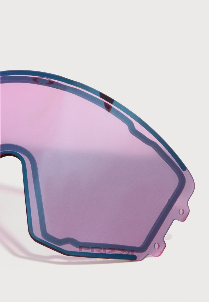 Primer plano parcial de una lente de gafas de sol curvada con tono púrpura, contorno negro y pequeños orificios de sujeción en un borde.