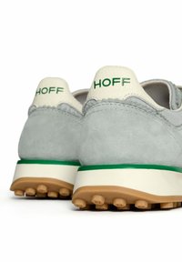 Baskets en suede gris avec des accents en cuir blanc et un branding vert. Semelle en caoutchouc épais avec un fond texturé marron. Design simple et fonctionnel.